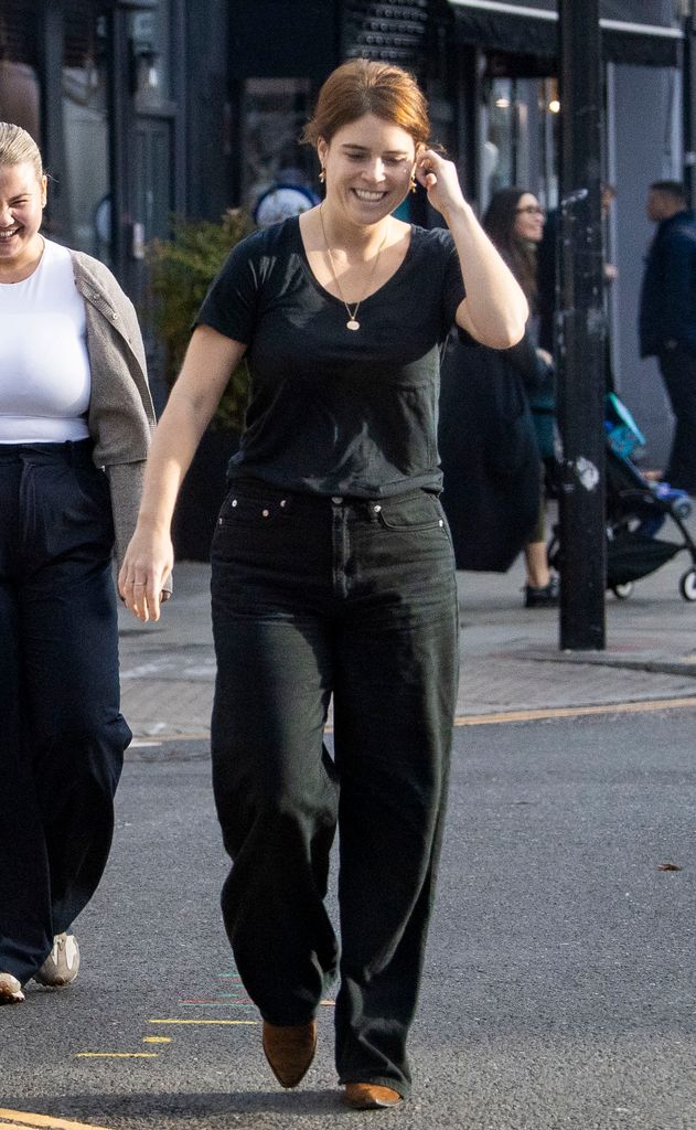 Princess Eugenie smiling and walking with a hand behind her ear