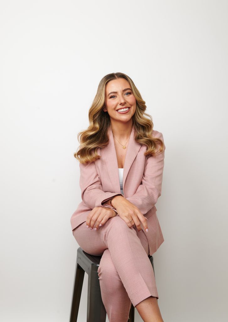 Woman with beautiful hair sitting and smiling wearing a pink suit