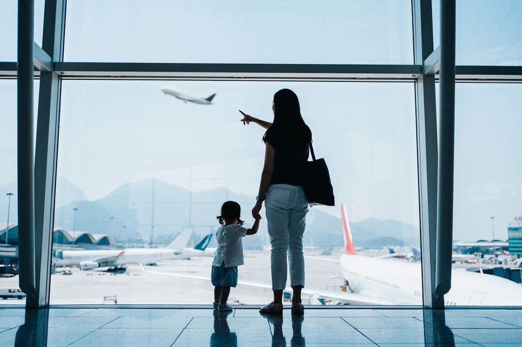 Une femme tenant la main d'un nourrisson et pointant un avion qui décolle à l'intérieur d'un aéroport