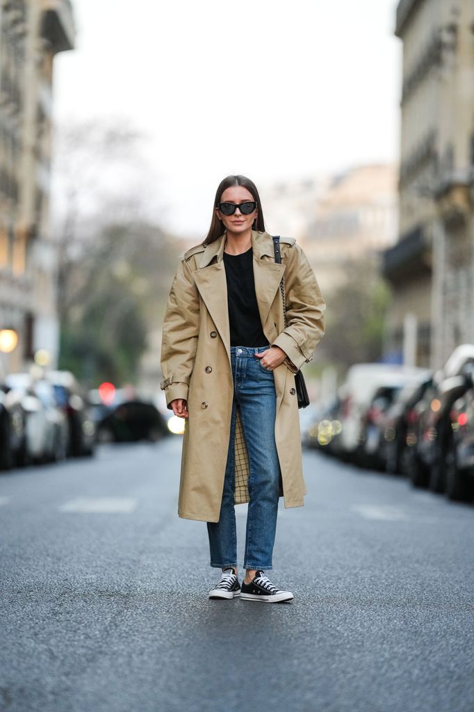 Diane Batoukina wears black sunglasses from YSL / Yves Saint Laurent, a black t-shirt, a beige long belted trench coat from Maison Margiela, a black shiny quilted / grained leather Boy shoulder bag from Chanel, blue denim cigarette pants from Massimo Dutti, black Converse sneakers, during a street style fashion photo session, on March 23, 2022 in Paris, France. (Photo by Edward Berthelot/Getty Images)