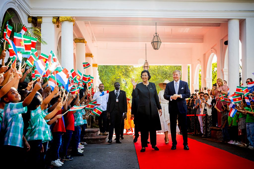 King Willem-Alexander and Queen Maxima walking down aisle with people waving flags
