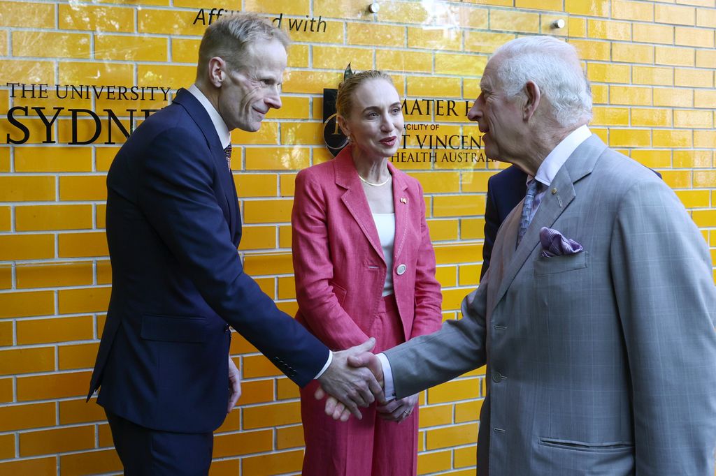 King Charles III (R) is greeted by co-medical directors Georgina Long (C) and Richard Scolyer (L)