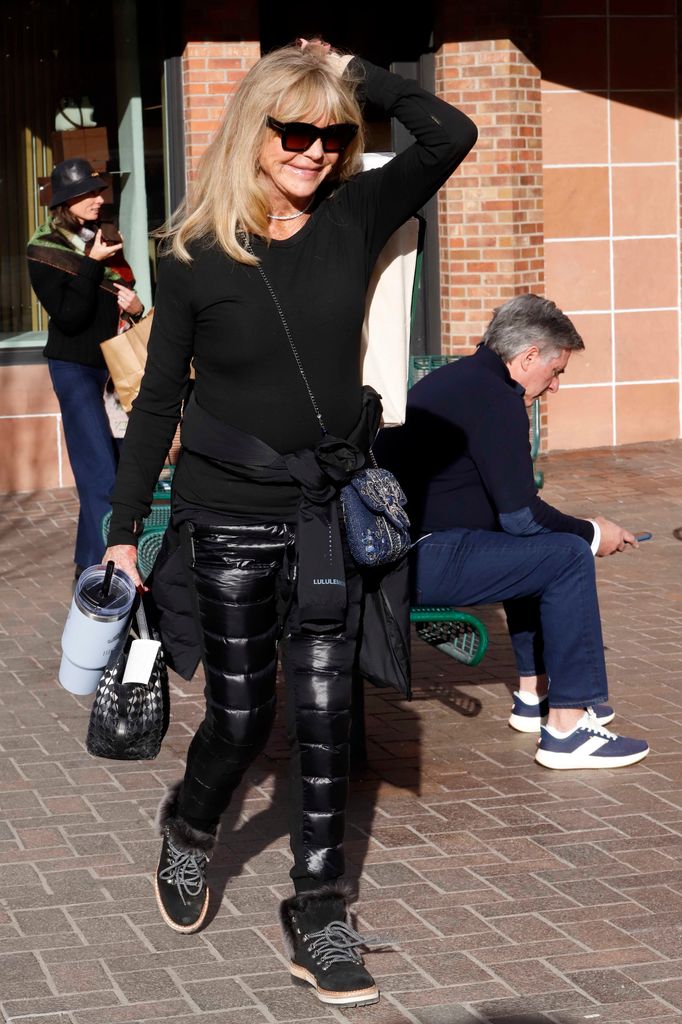 Goldie Hawn in black ski outfit and sunglasses walking outside