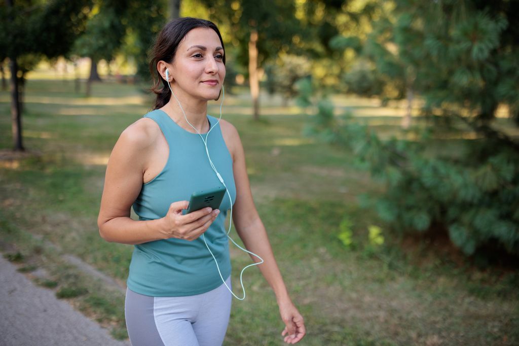 A mid adult woman listening to music while walking in a public park