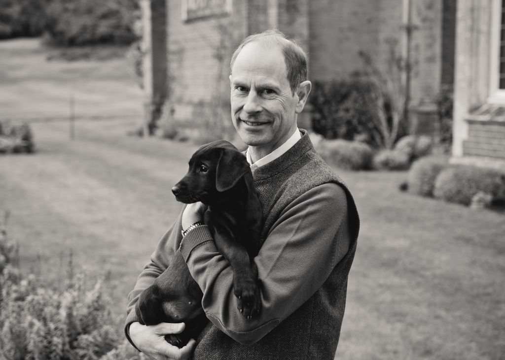 Black-and-white photo of Prince Edward holding a black puppy