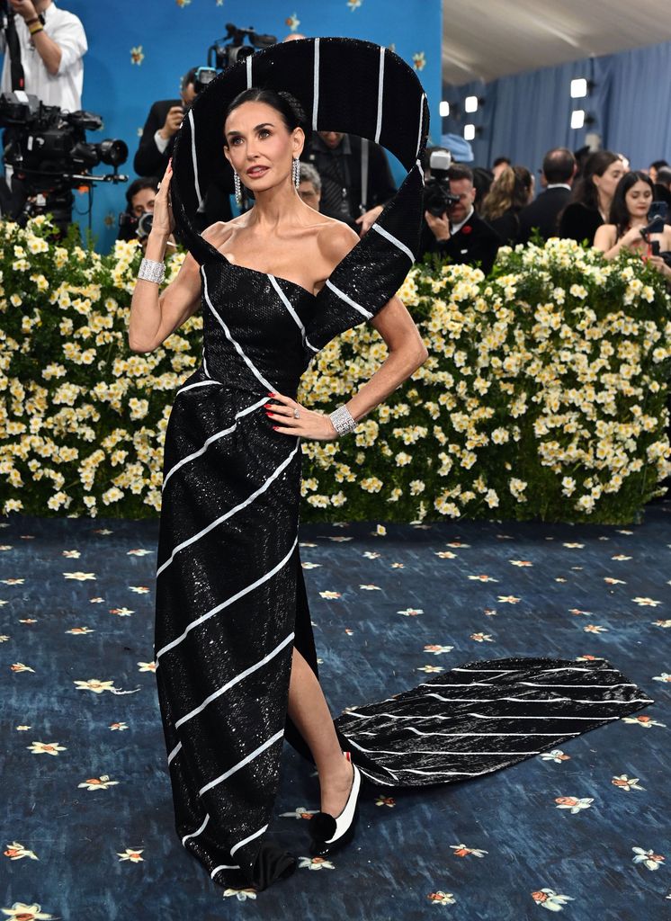 Demi Moore wears a black and white striped dress with sculptural detailing and matching black and white shoes.