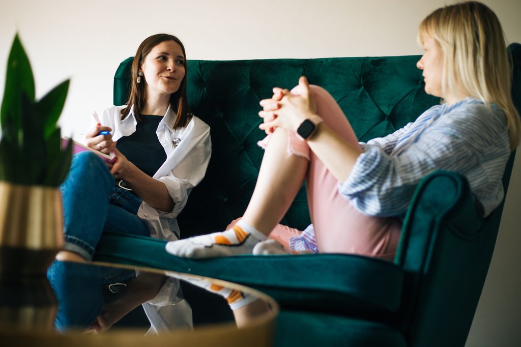 Safe space to deal with menopause issues and aging problems: Middle-aged female psychotherapist and mature female patient sitting on green couch communicating while looking at each other