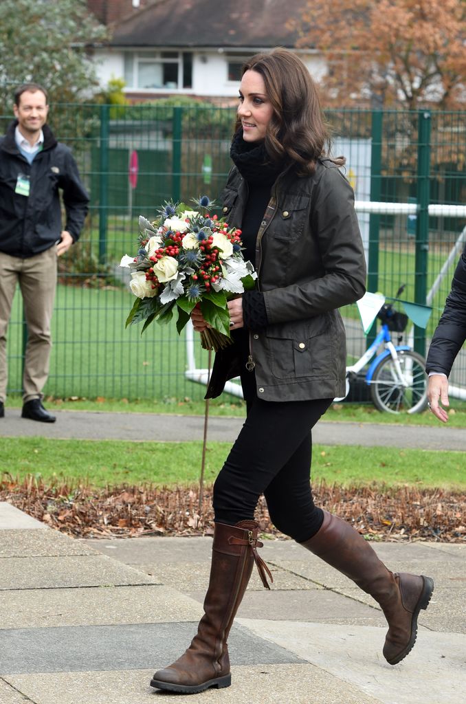 Kate in school playground holding flowers in flat boots and waxed jacket