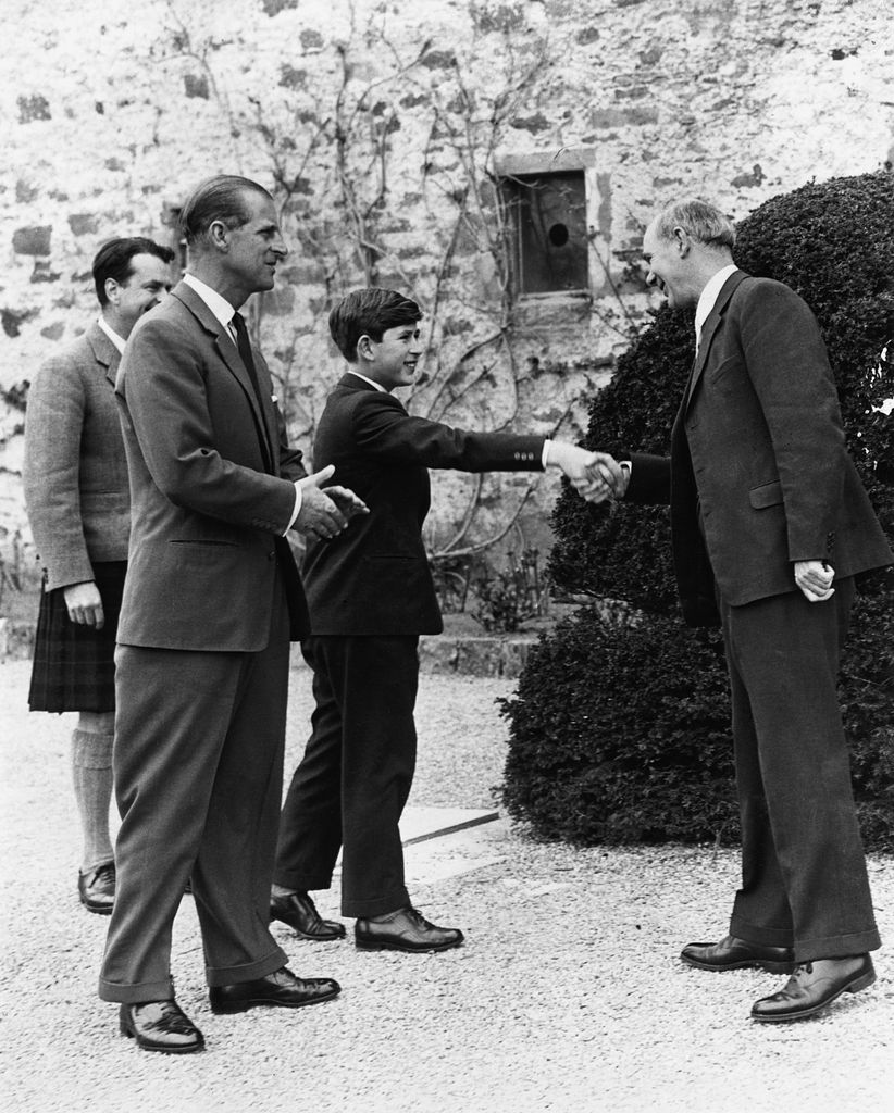 King Charles shaking hands with a headmaster with Prince Philip by his side