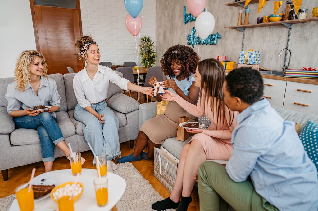 Beautiful young pregnant black woman having a baby shower with friends at home. Opening up gifts she received