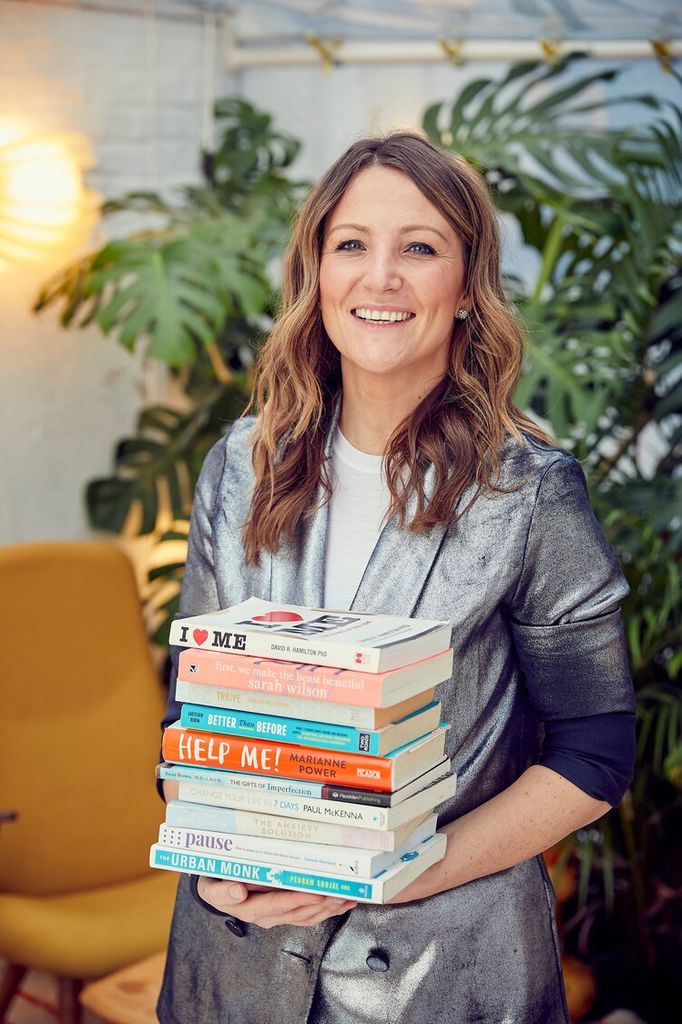woman smiling while holding a pile of books 