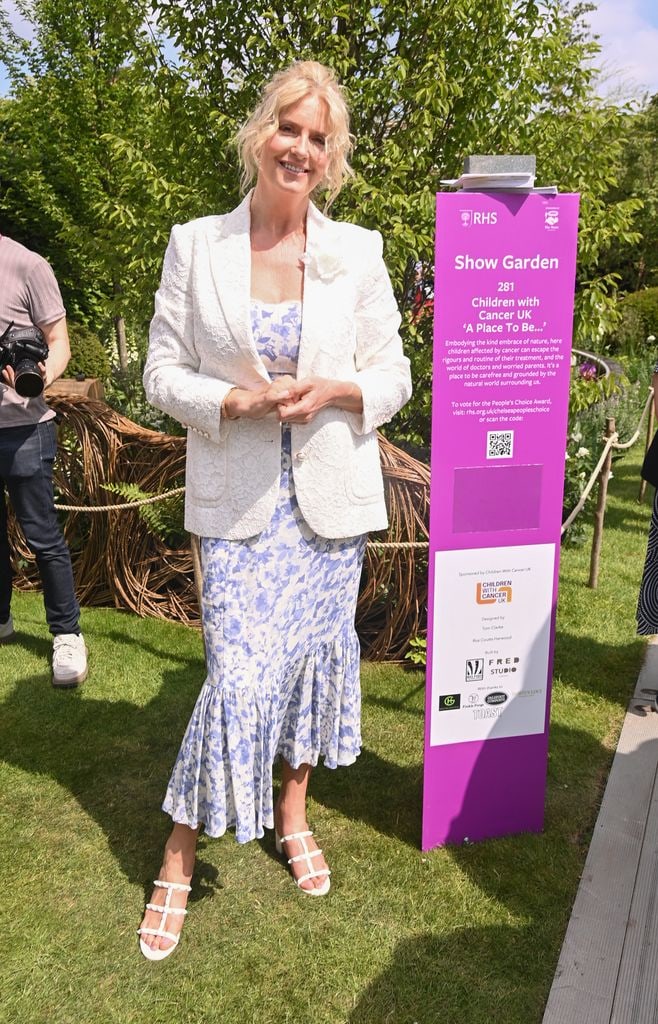 Penny Lancaster at Chelsea Flower Show 2025 in a white and blue floral dress with ruffle hem, ivory textured blazer and white sandals