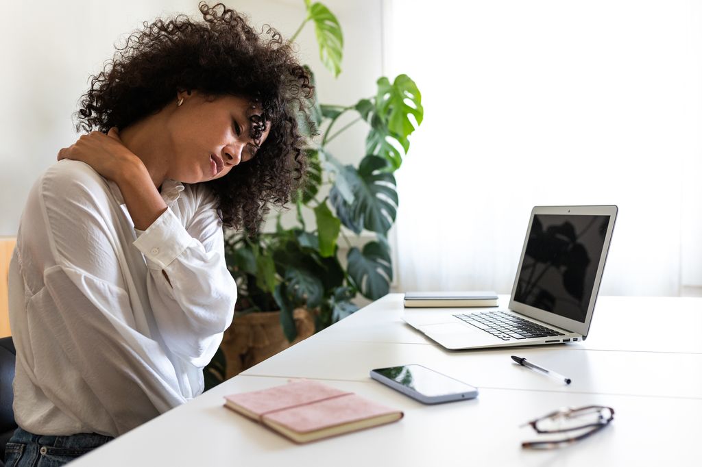 African American woman suffering from neck pain. Hispanic female working with laptop at home self massaging neck and shoulders.