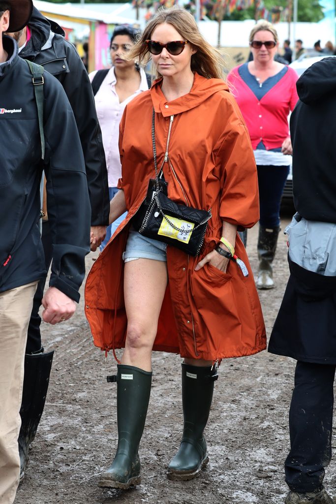 Stella McCartney attends the Glastonbury Festival in 2016 wearing a bright orange raincoat and mini denim shorts 