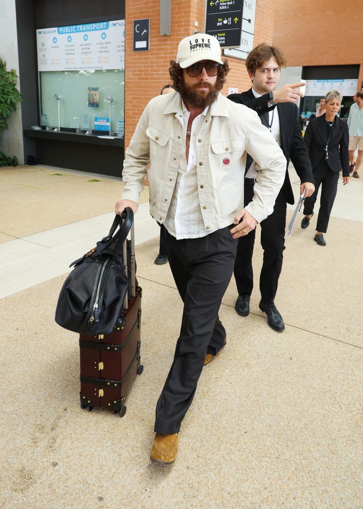photo of aaron taylor johnson wheeling suitcase with bushy beard and longer hair