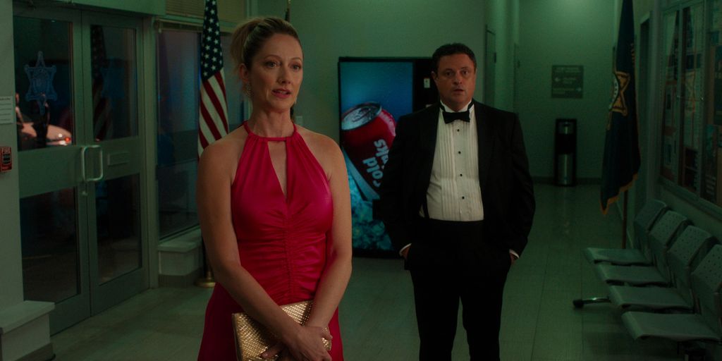 woman in red dress standing in front of man in tuxedo in dimly-lit hall 