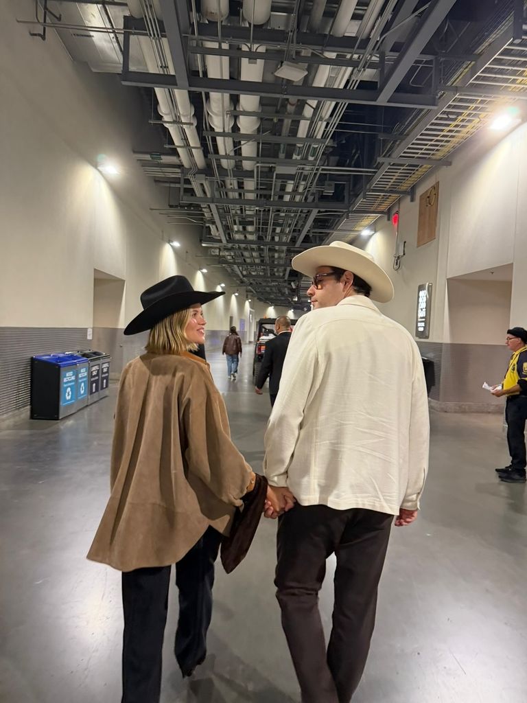 Sofia Richie and Elliot Grainge in matching cowboy hats. Sofia wears a logn brown shirt, Elliot a long cream shirt. They both walk away from the camera and look at each other