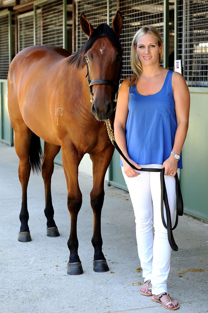 Zara Tindall sorrindo em um vestido branco e blusa azul com um cavalo