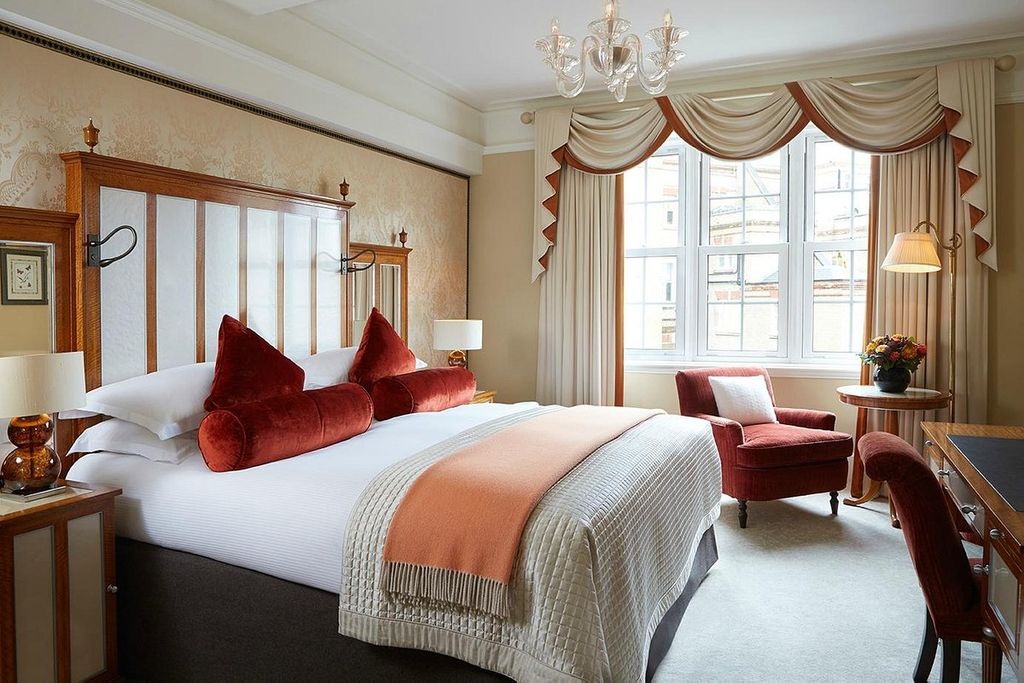 An ornate hotel room with orange bolster cushions, white sheets and a burnt orange armchair
