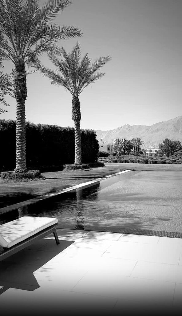 Swimming pool is in focus surrounded by palm trees and mountains in the background