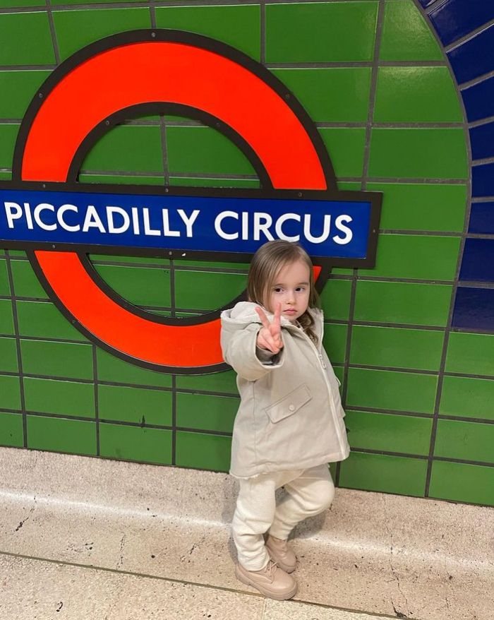 A young girl flashing the peace sign with a Piccadilly Circus roundel behind her