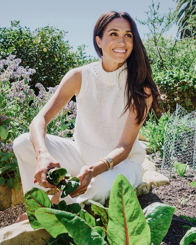 Meghan picking up some leaves from her garden, looking up and smiling 
