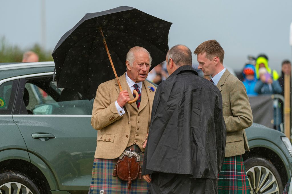 King Charles in a kilt holding a black umbrella