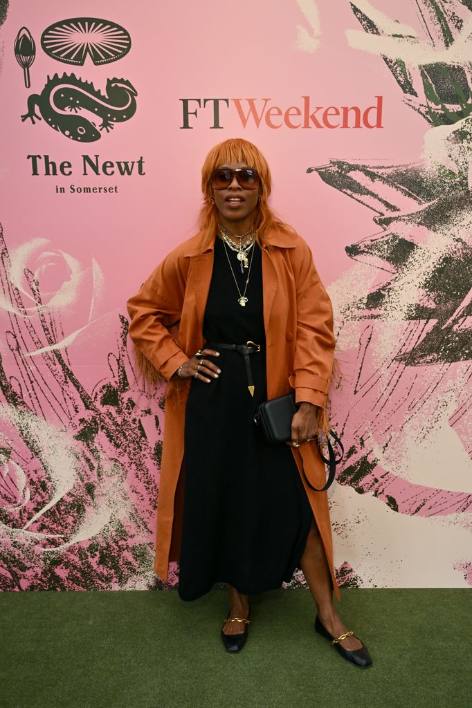 Susan Bender Whitfield wears a burnt orange coat over a black dress with statement jewellery and black flats at FT Weekend x The Newt party at the Chelsea Flower Show