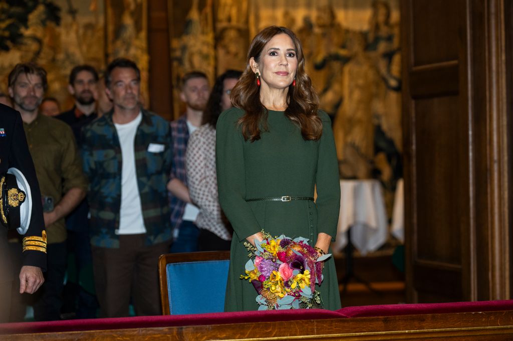 Queen Mary in dark green dress with vibrant earrings