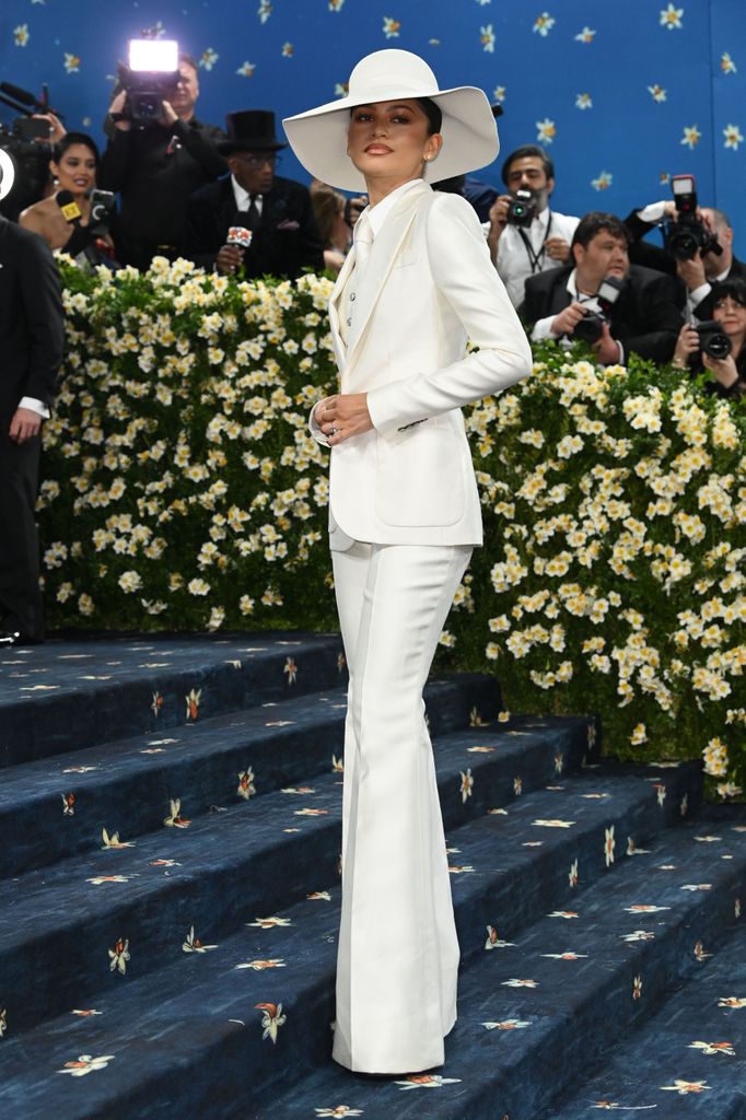 Zendaya wears a white three piece suit with flared trousers and a matching hat