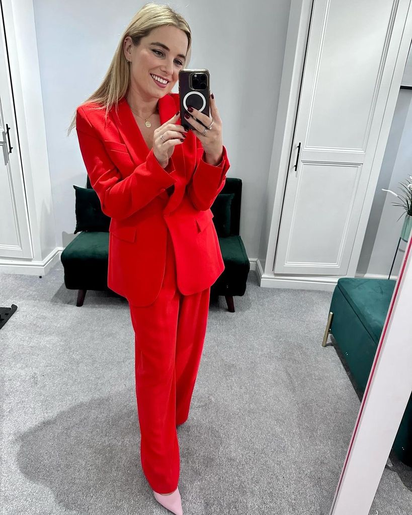 Sian Welby tira selfie no espelho em terno vermelho no camarim de casa
