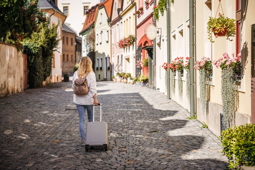 Solo travel. Woman tourist with suitcase and backpack walking on street