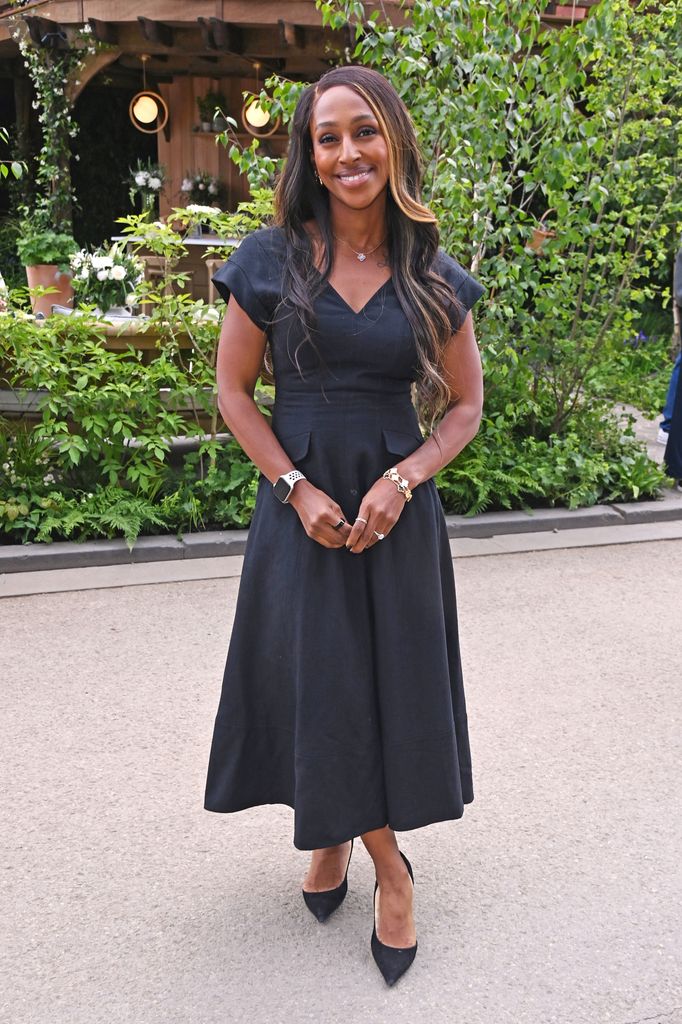 Alexandra Burke in a black midi dress and heels at the Chelsea Flower Show, accessorised with an Apple Watch and gold jewellery.