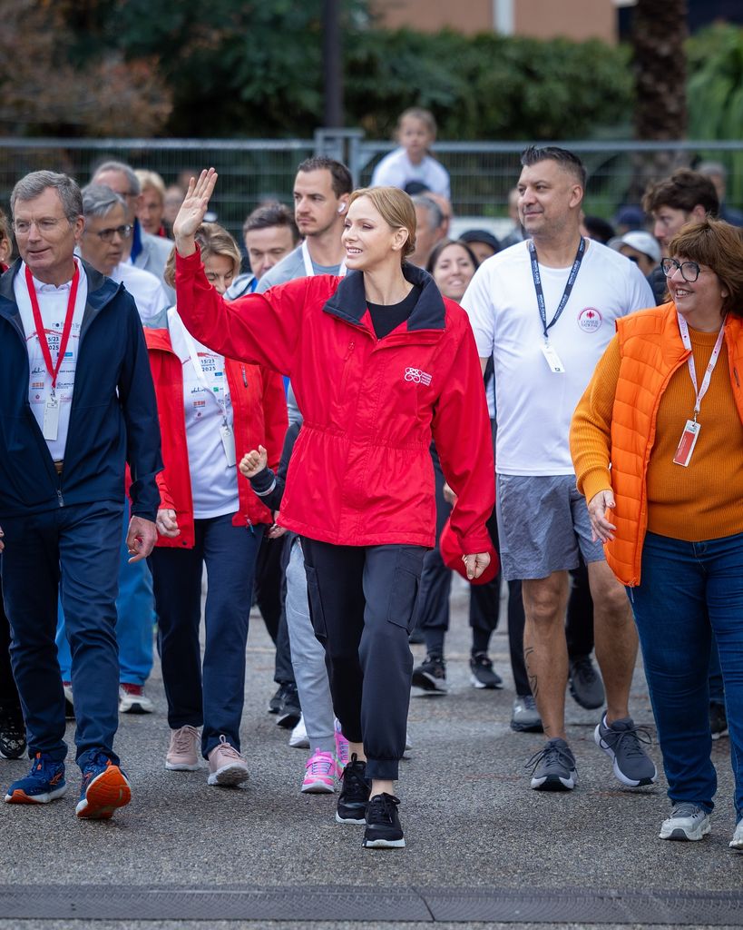 princess charlene waving in red coat leading group walk