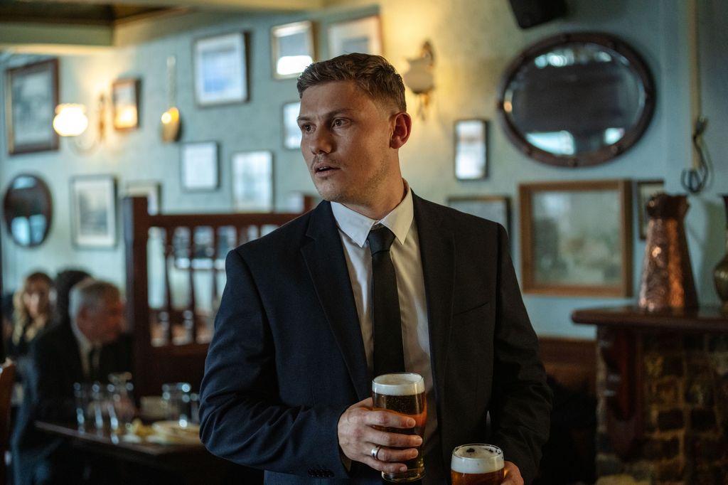 man in suit holding beers in pub