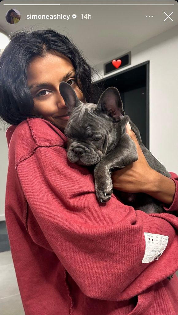 Simone Ashley in red jumped holding a dog