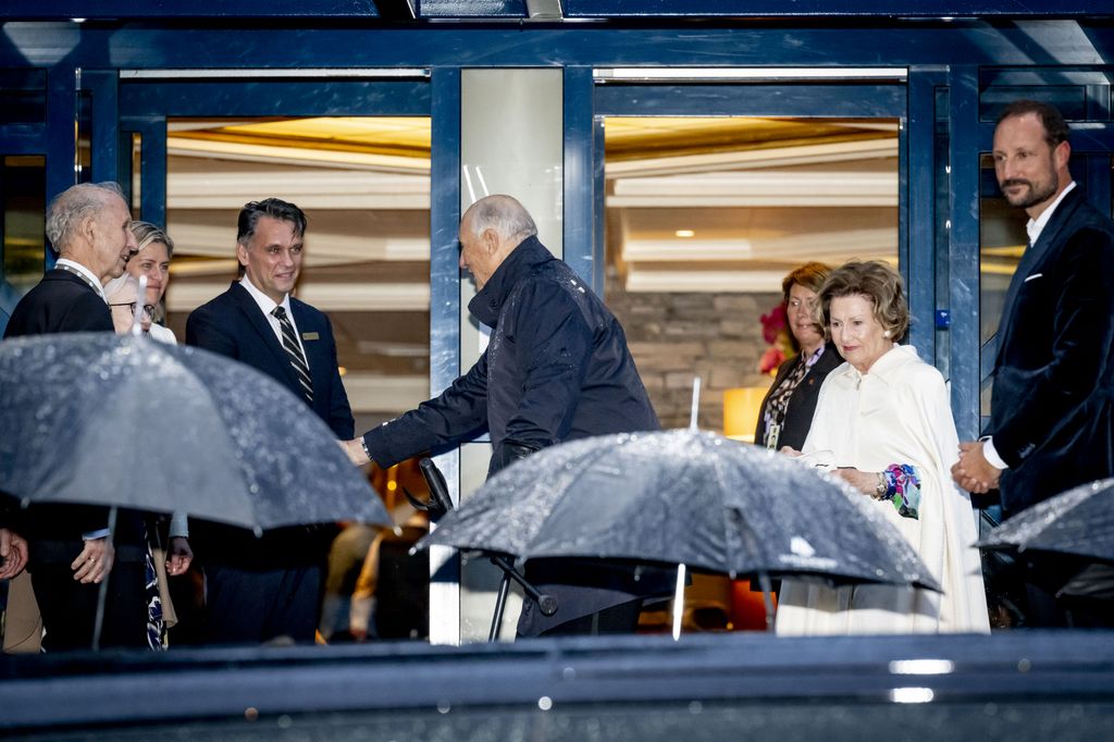 King Harald shaking a man's hand with Queen Sonja and Crown Prince Haakon behind him