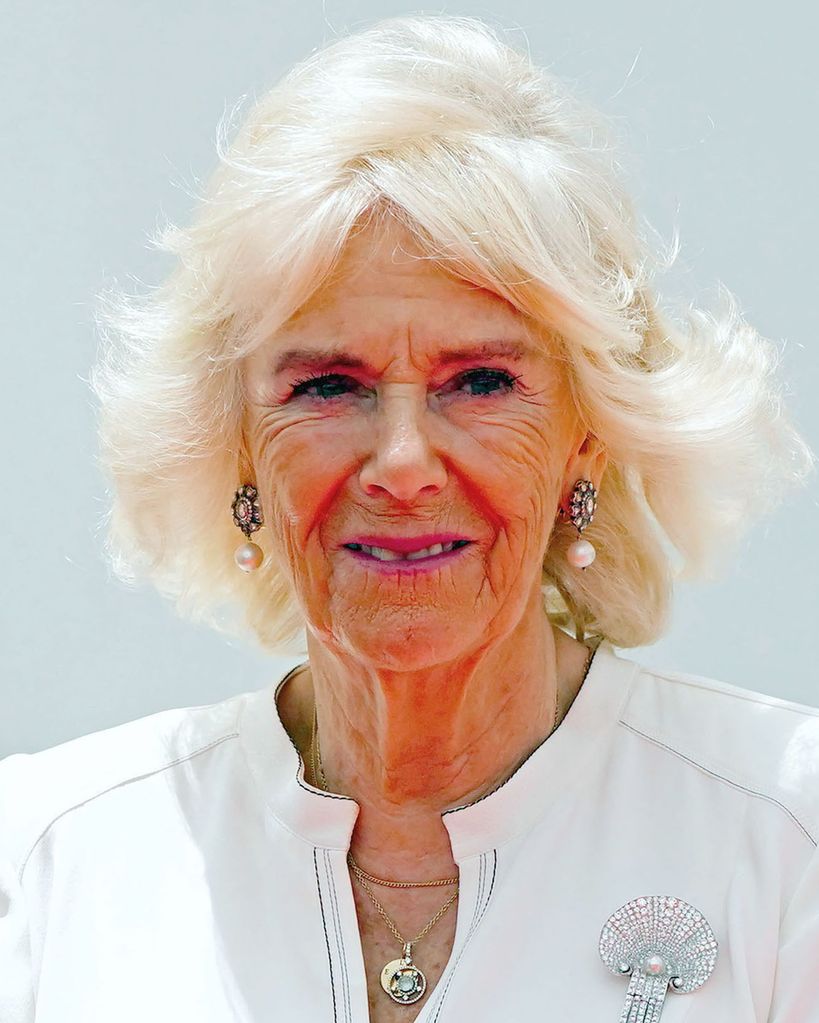 Queen Camilla smiling whilst wearing a white dress and diamond earrings