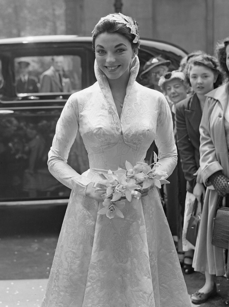 English actress Joan Collins smiling in a high collared wedding dress