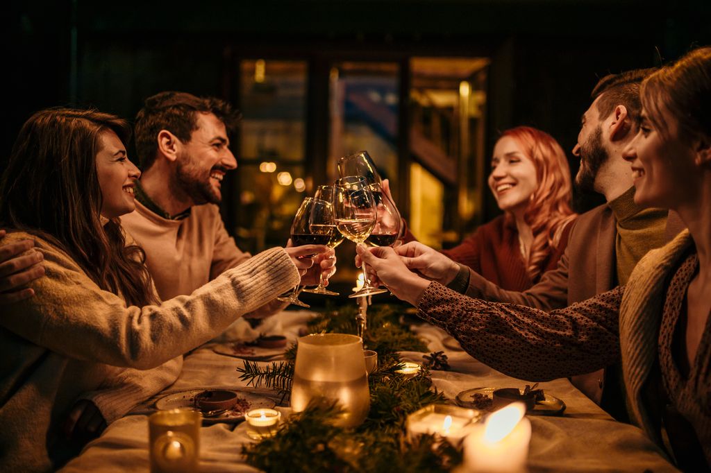 Group of elegantly dressed friends having a small boho dinner/wedding outdoors in a garden, drinking wine, and talking to each other with a great mood and smiles.