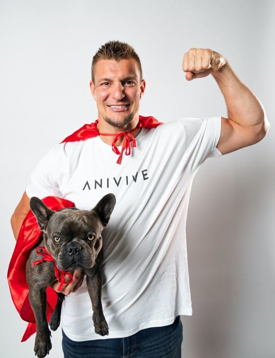 Gronk wears a red cape and hold his Frenchie Ralphie 
