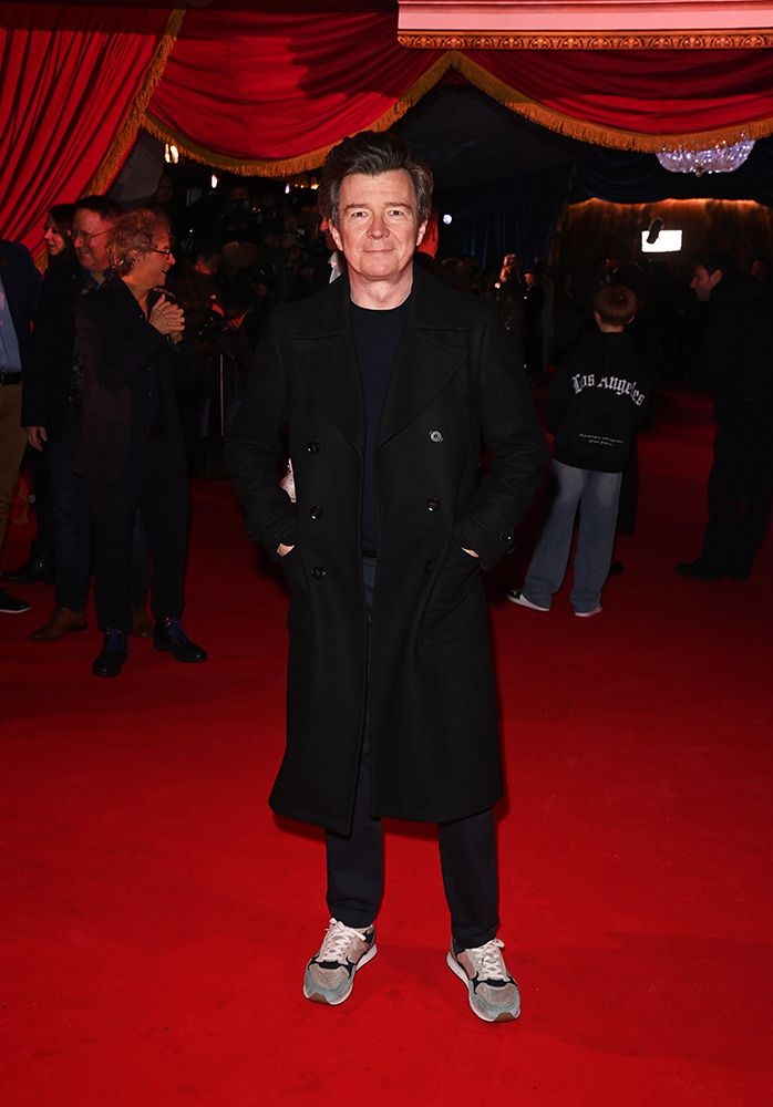 Rick Astley wearing a black coat and trousers on the red carpet 