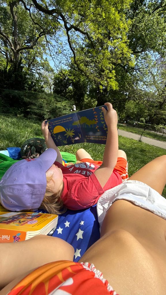 Emily Ratajkowski lying down next to her son, wearing a tiny white frilled skirt paired with an orange bikini top.