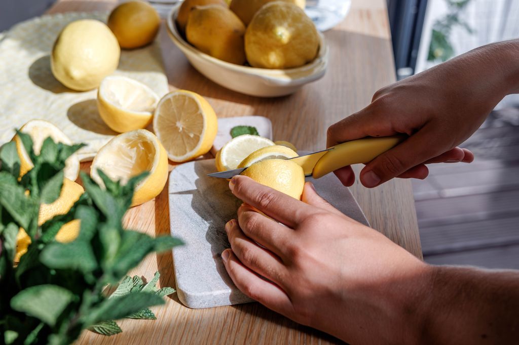 Side view of hands cutting slices of lemon on a chopping board in the kitchen