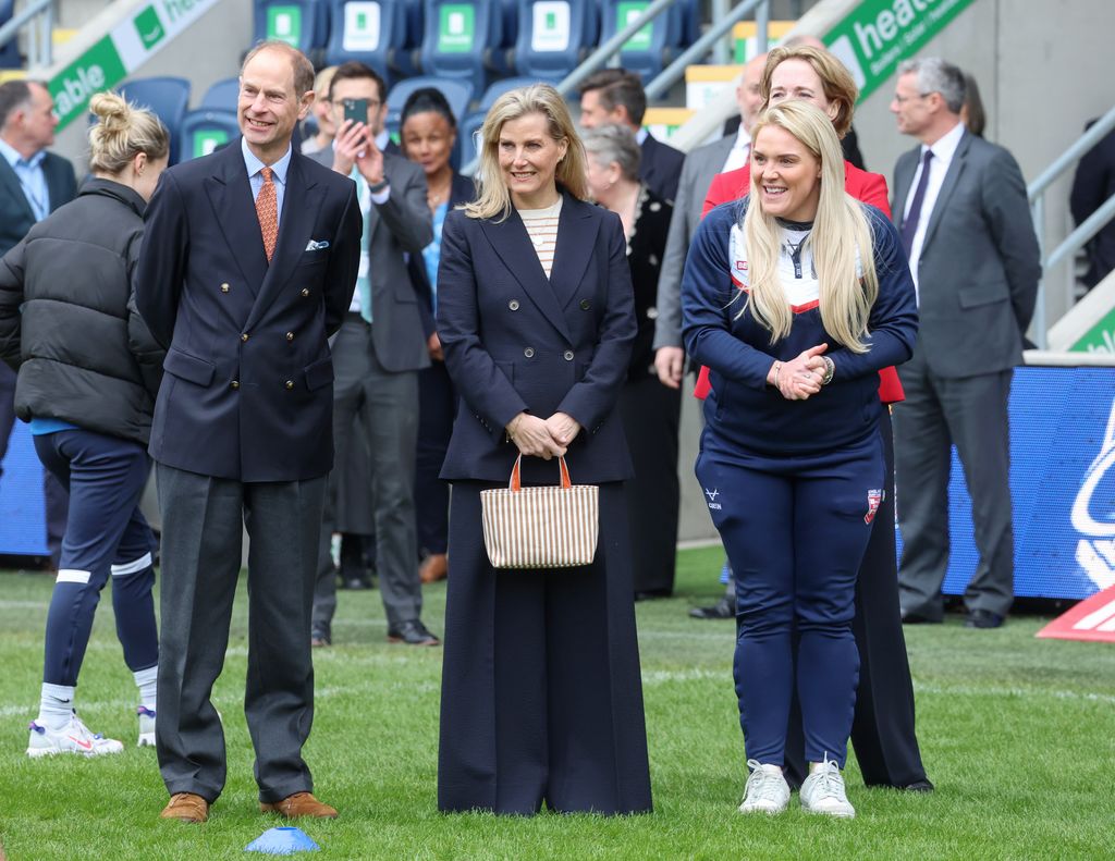 Sophie and Edward in coordinating navy suits on rugby pitch