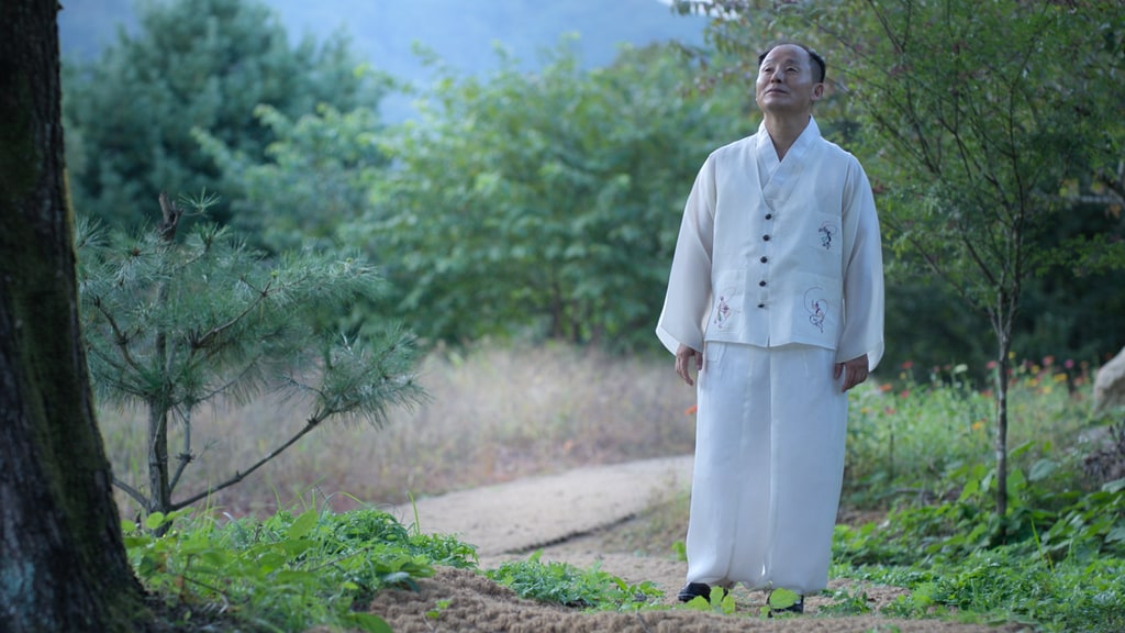 Man in white outfit looking serene as he walks in nature 