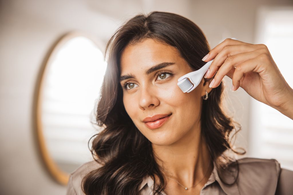 Young woman looking in mirror and using micro needle meso derma Roller.
