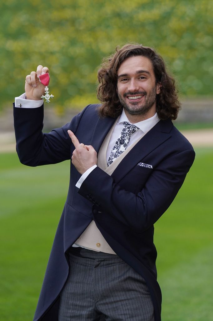 Joe Wicks in a suit pointing at his MBE