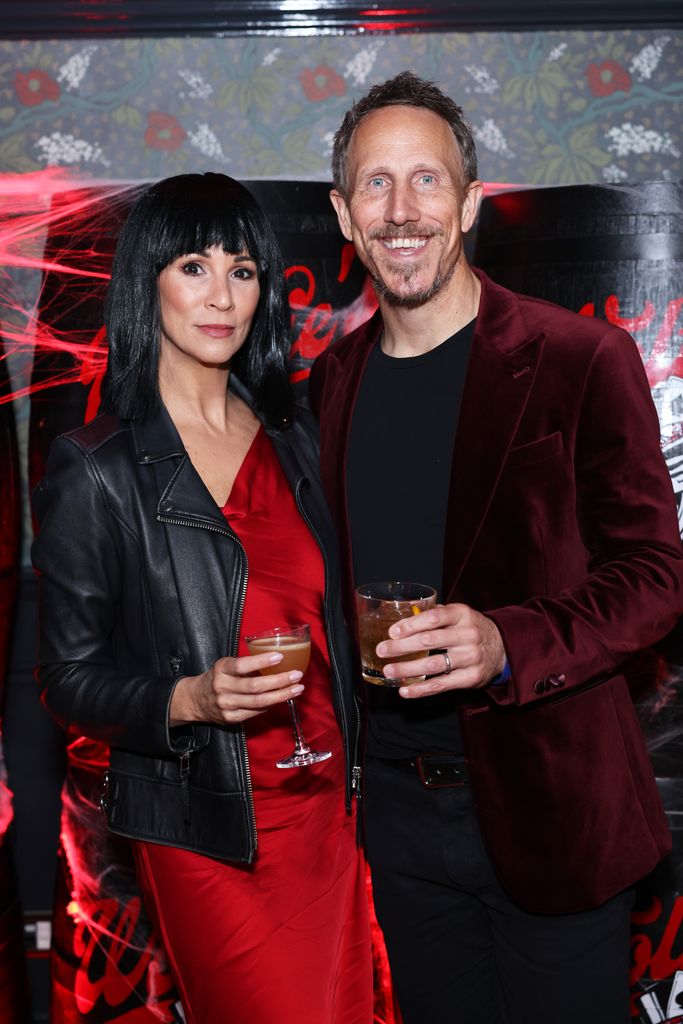 Andrea McClean  in red dress and leather jacket with partner