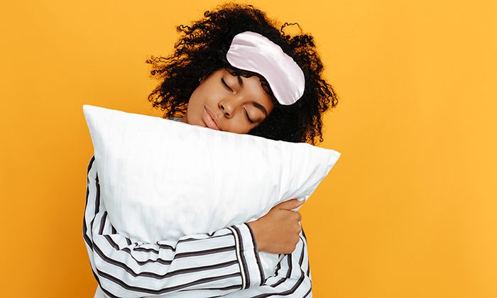 Woman with an eye mask on her head hugging a pillow